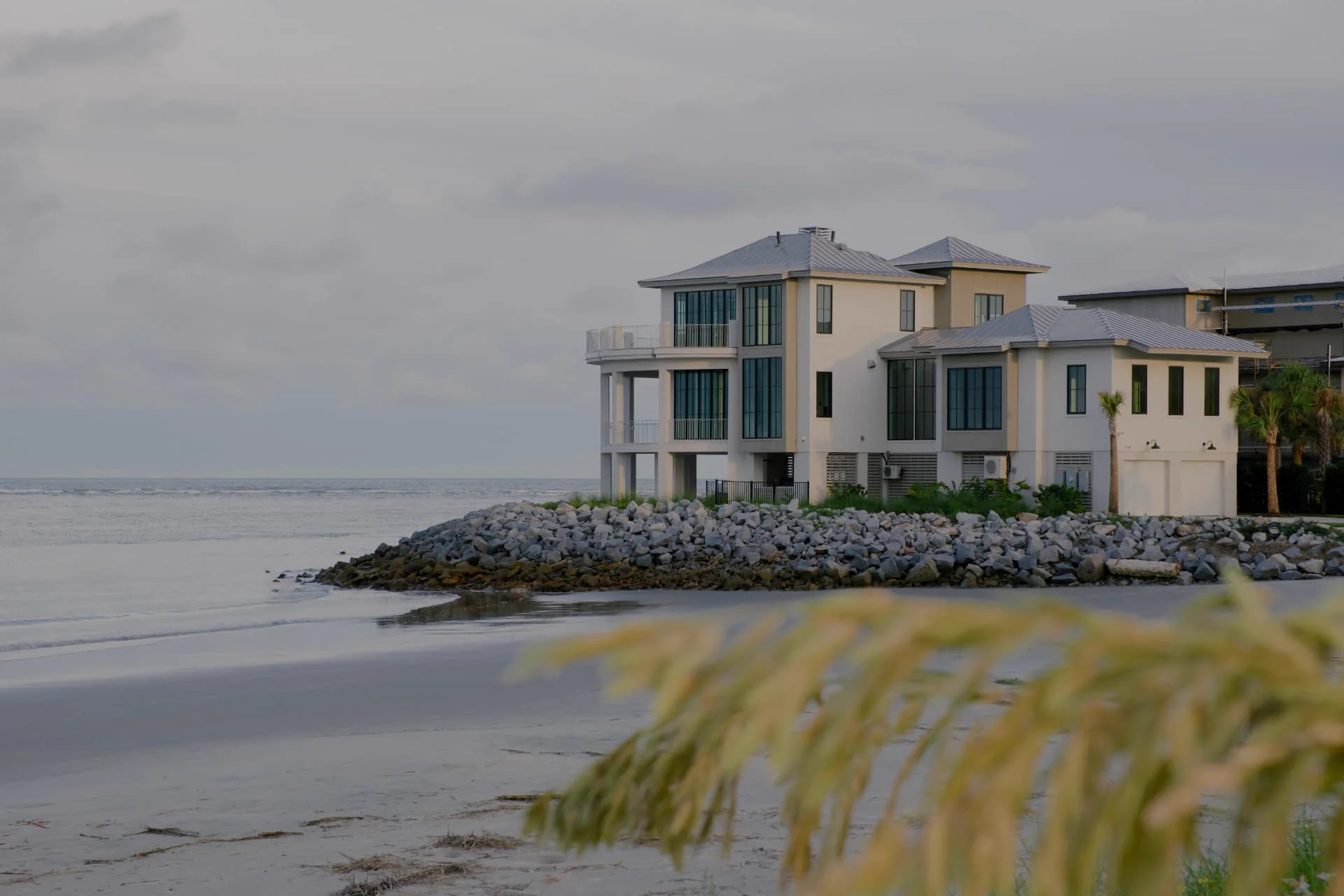 Modern beachfront home beside the ocean under a soft gray sky